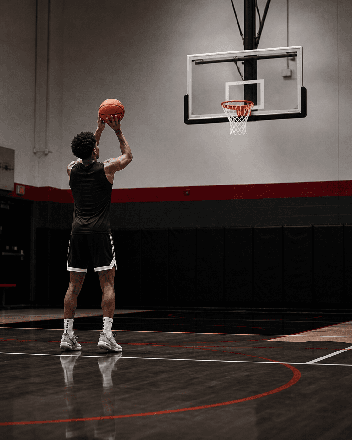 College basketball player facing the basket while practicing free throws alone in a local indoor gym.
